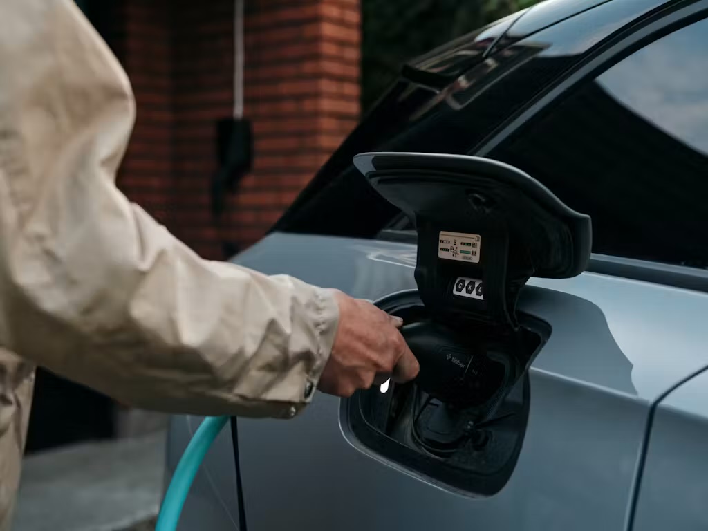 Close-up van een hand die een laadstekker in de laadklep van een elektrische auto steekt • beeld uit de gezamenlijke perskit van Tibber en Joulo